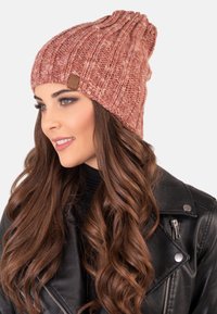Gorro de punto en un cálido tono rosado con acanalado vertical y una etiqueta de cuero marrón. Textura suave con un diseño holgado.