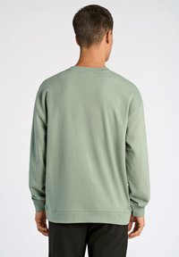 Bluza z długim rękawem i okrągłym dekoltem w stonowanym zielonym kolorze, wykonana z miękkiej bawełny. Posiada luźny krój, ściągacze na mankietach oraz prosty dół.