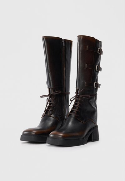 Brown leather knee-high boots with a textured finish, lace-up front, side zipper, and three adjustable buckled straps. Block heels.