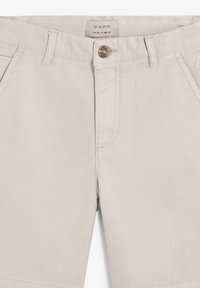 Shorts décontractés beige avec fermeture à bouton, passants pour ceinture, poches avant, et une étiquette indiquant la taille 38 et la marque Scalpers.