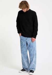 Black knit sweater, relaxed fit, round neckline. Light blue wide-leg jeans with a faded wash. Black sneakers with white soles.