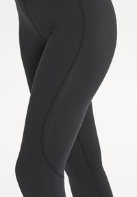 Schwarze Leggings aus glattem, dehnbarem Stoff mit gewölbten Nahtdetails, einem taillierten Design und ohne sichtbare Beschläge oder Muster.