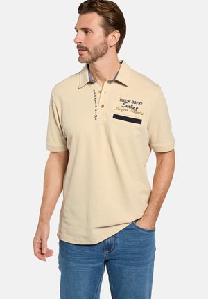 Beige Poloshirt mit Kragen, kurzen Ärmeln und dekorativer Stickerei. Enthält eine marineblaue Tasche und gestickte Textelemente.
