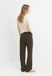 Maglione beige chiaro con maniche lunghe abbinato a pantaloni a gamba larga marroni scuri e calzature chiare. Texture minimaliste e lisce.