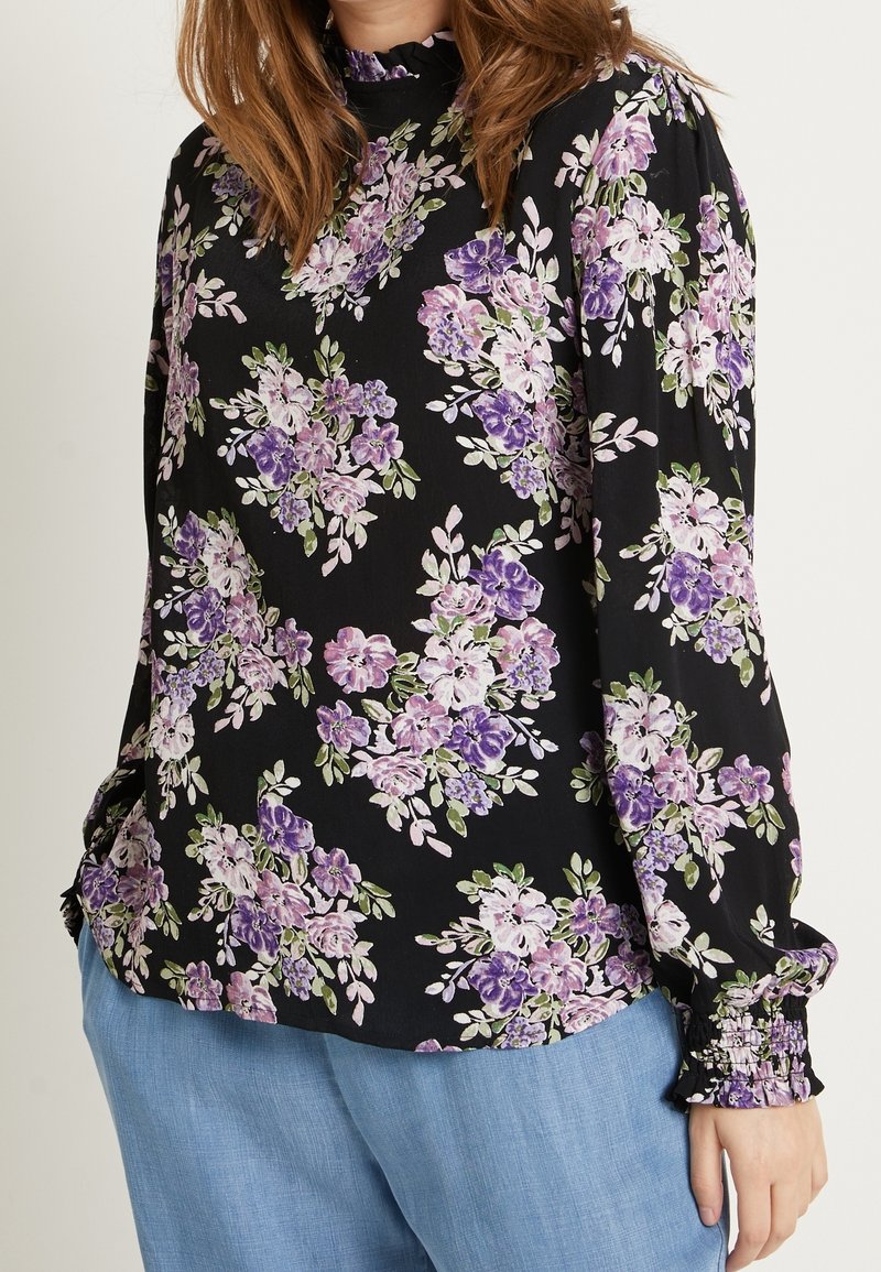 Langærmet bluse i sort stof med et blomsterprint i lilla og grøn. Rynket udskæring og samlede manchetter. Løs pasform.