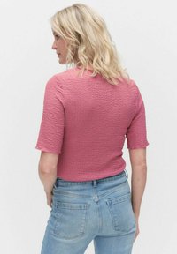 Krótki rękaw, teksturowana bluzka w kolorze różowym, o dopasowanym kroju. W połączeniu z dżinsami o średnim zmyciu, stylizacja ma charakter casualowy.