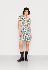 Vestido de manga curta com estampa floral tropical em tons de verde, rosa e amarelo; possui um corpete justo e uma saia rodada. Botas de combate pretas.