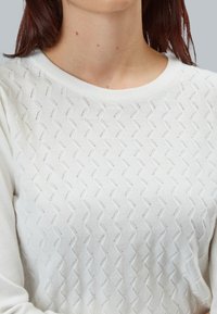 Maglione bianco lavorato a maglia con motivo zigzag, scollo rotondo e maniche lunghe. La texture è morbida con dettagli a tessitura aperta.