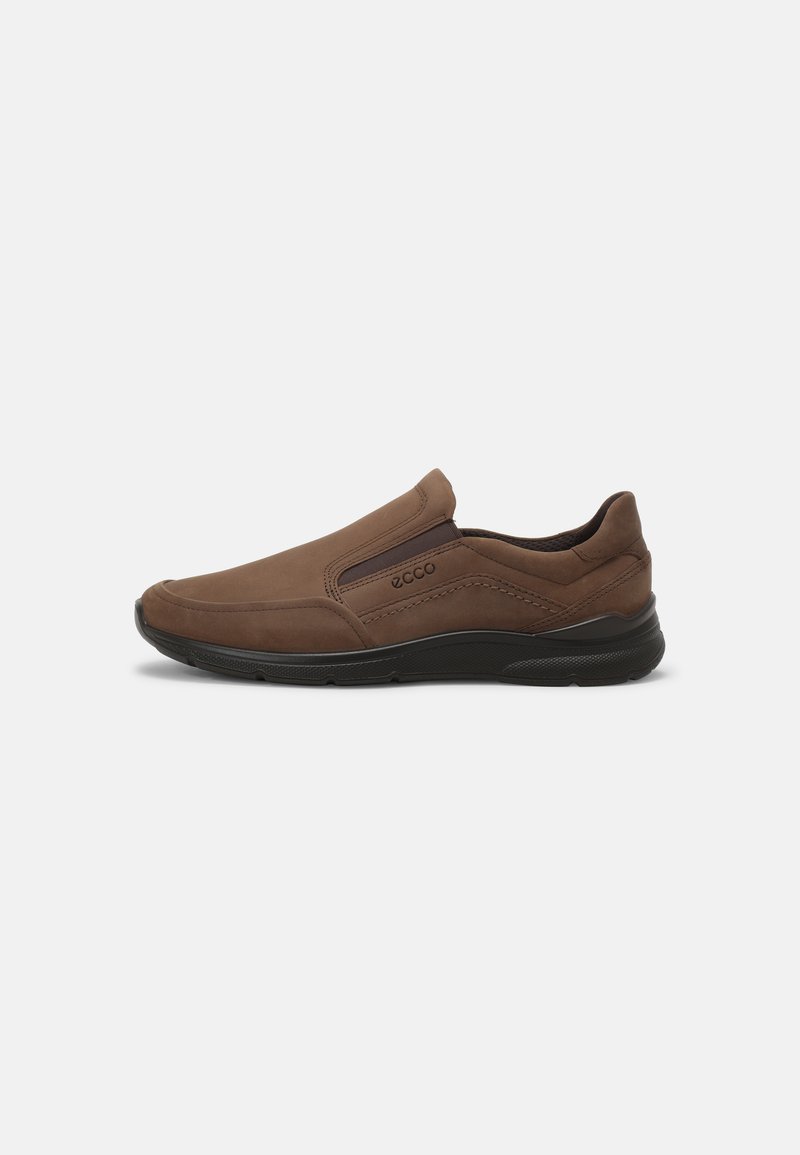 Barna, velúrból készült, sima textúrájú, slip-on cipő, párnázott nyakkal és gumitalppal a tapadása érdekében. Oldalán diszkrét logóval rendelkezik.
