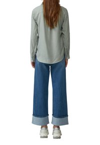 Chemise à rayures vertes à boutons, à manches longues, associée à un jean bleu à jambes larges avec un double revers, et des baskets blanches.