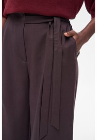Ciemnobrązowe spodnie o szerokich nogawkach z paskiem w talii, wykonane z gładkiego materiału, posiadające boczne kieszenie, zaprojektowane na luźny krój.