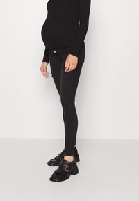 Svarta gravid skinny jeans med slitna detaljer, som matchar med svarta klackiga loafers med fransar och spännen. Långärmad svart topp.