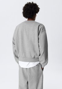 Grijze sweatshirt met een cropped ontwerp, geribbelde manchetten en zoom. Zachte textuur. Draag over een witte laag, met zijzakken op de broek.