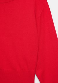 Pull en tricot rouge vif à manches longues avec ourlet et poignets côtelés, montrant le haut du torse et une manche sur un fond uni.