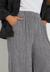 Grå ribbade byxor med avslappnad passform, med sidofickor och elastisk midja. Kombineras med en svart denimjacka.