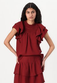 Top bordeaux froncé avec un col smocké et des manches courtes, fabriqué en tissu léger, présentant une silhouette décontractée et des accents texturés.