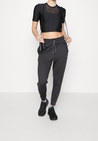 Czarny krótki top z siateczkowym panelem, zestawiony z szarymi dresami z regulowanym paskiem w talii. Czarne sportowe buty z teksturowaną podeszwą.