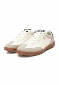 Zapatillas de ante beige y cuero blanco con cordones planos, suela de goma y acentos negros en el talón y la lengüeta. Diseño atlético clásico.