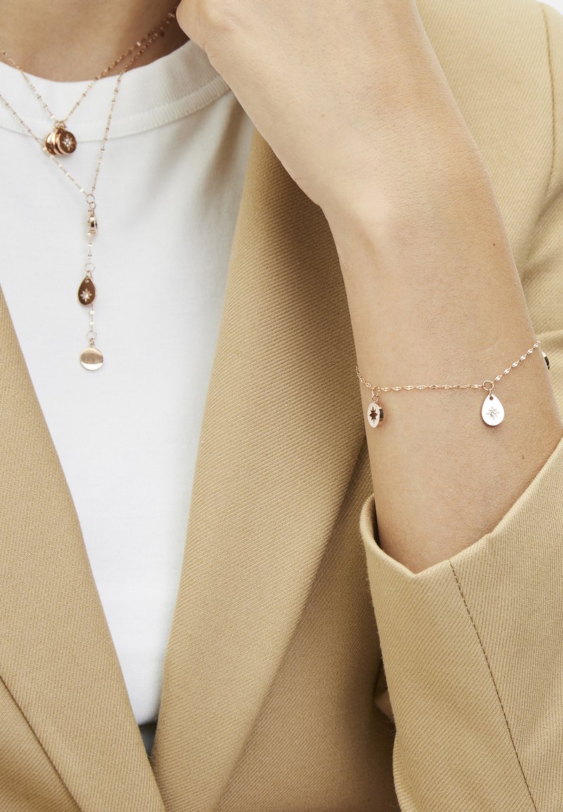 Gold-toned layered necklaces with teardrop and circular pendants; matching bracelet with similar design, featuring tiny charms and a delicate chain.