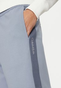 Shorts de color azul claro con una tela texturizada, que presentan un bolsillo lateral y un panel de acento en azul más oscuro con el logo "Calvin Klein" bordado.