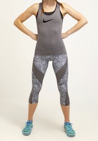 Gray athletic tank top with black logo, patterned gray leggings, and light blue running shoes. Leggings feature geometric designs and textured accents.