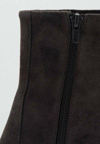 Bottine en daim marron foncé avec une fermeture éclair centrale noire, présentant une texture lisse et des lignes épurées, mettant en valeur son design minimaliste.