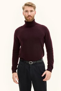 Bordeauxfarbener Rollkragenpullover aus weichem Material, figurbetontes Design mit langen Ärmeln. Kombiniert mit schwarzer Hose und Gürtel mit silberner Schnalle.