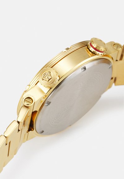 Montre dorée avec un boîtier en métal poli, ornement en tête de lion sculptée, fond en acier inoxydable et un design de bracelet classique à maillons.