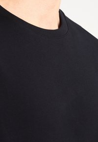 Camiseta de algodón negra con cuello redondo, textura suave y mangas cortas, centrada en su diseño simple y versátil.