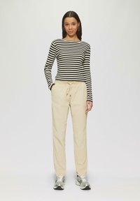 Gestreepte zwart en crèmekleurige lange mouwen shirt, gecombineerd met beige broek met elastische tailleband. Model draagt grijze sneakers. Eenvoudige, casual look.