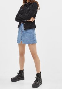 Černá džínová bunda, světle modrá džínová sukně s rozparkem vpředu a černé šněrovací bojové boty s robustní podrážkou.