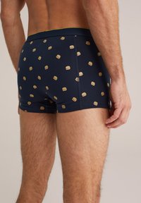 Sötétkék boxer alsónadrág sima anyagból, ismétlődő hamburger mintával, arany elasztikus derékpánttal és testhezálló fazonnal.