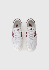 Hvite lær sneakers med maroon aksenter, med perforerte tær og snøring. Merkbar "NB" logo på tungen.