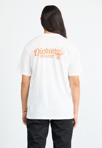 Witte katoenen t-shirt met oranje grafische tekst en ontwerp op de achterkant. Ronde hals en korte mouwen, ontspannen pasvorm.