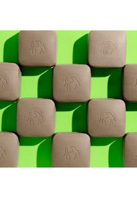 Brown square soaps with a smooth texture, featuring an embossed elephant design, arranged in a grid on a bright green background.