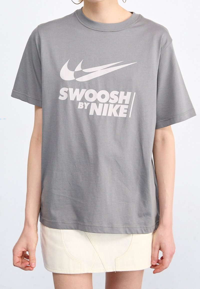 Šedé bavlněné tričko s kulatým výstřihem, krátkými rukávy a bílým logem a textem Nike vytištěným na přední straně.