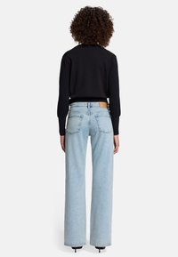 Maglione nero a maglia con polsini a costine abbinato a jeans a gamba larga blu chiaro, caratterizzato da una toppa in pelle color tan sulla cintura posteriore.