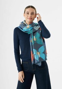 Écharpe multicolore avec un motif de papillon dans des nuances de bleu, d'orange et de rose, fabriquée en matériau doux, tombant élégamment autour du cou du modèle.