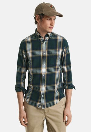 Chemise à carreaux vert et bleu marine avec col boutonné et manches retroussées, assortie à une casquette beige ornée d'un motif brodé coloré.