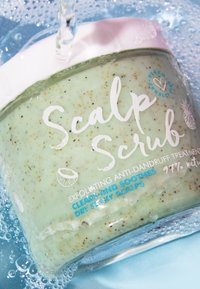 Groene hoofdhuid scrub in een heldere pot met een witte deksel, met exfoliërende deeltjes. De labeltekst beschrijft een anti-roos behandeling en natuurlijke ingrediënten.