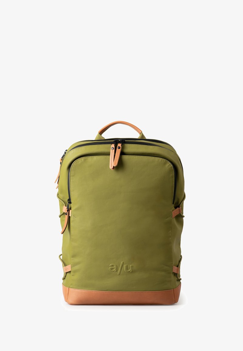 Zaino verde oliva con texture liscia, zip nere, dettagli in pelle beige e un logo prominente alla base. Presenta cinghie laterali.