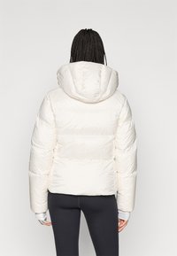 Biely puffový kabát s kapucňou, so štýlovým prešívaným dizajnom a priliehavým strihom. Mäkká, hladká tkanina s rebrovanými manžetami a skráteným strihom.
