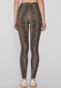 Legginsy w panterkę z dopasowanym krojem, elastycznym materiałem i wysokim stanem. Tekstura jest gładka, z ciemnobrązowymi i beżowymi wzorami.