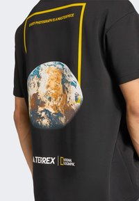 Black t-shirt featuring a large, vibrant graphic of Earth, bordered by a yellow rectangle and text "EVERY PHOTOGRAPH IS A MASTERPIECE."