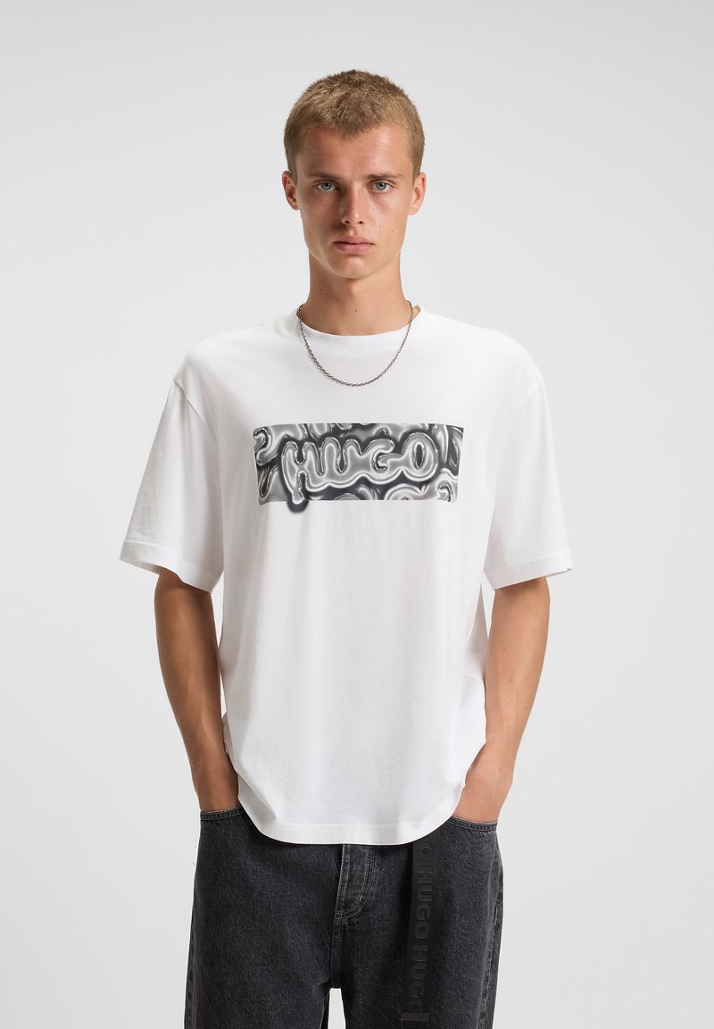 Hvid bomulds t-shirt med et vandret sort og sølv logo grafisk tryk. T-shirten har korte ærmer og en afslappet pasform.