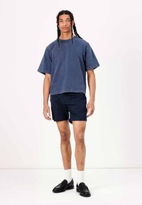 T-shirt surdimensionné en coton bleu marine, associé à un short bleu marine foncé. Porté avec des chaussettes blanches et des chaussures noires, arborant un style décontracté.