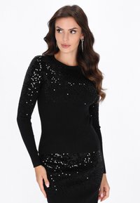 Schwarzer gerippter Pullover mit einem Pailletten-verzierten Design an den Schultern, langen Ärmeln und einer taillierten Form.