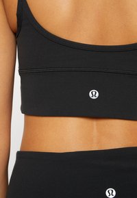 Czarny sportowy top crop z bezszwowym designem, z okrągłym dekoltem, cienkimi ramiączkami i małym logo na środku przodu.