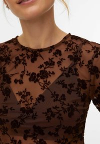 Haut marron transparent avec broderie florale foncée, encolure ronde et manches courtes, avec un dessus texturé et un tissu lisse en dessous.