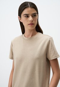 T-shirt beige a maniche corte con scollatura rotonda. Tessuto morbido con vestibilità rilassata e cuciture minime. Nessun motivo o grafica visibile.